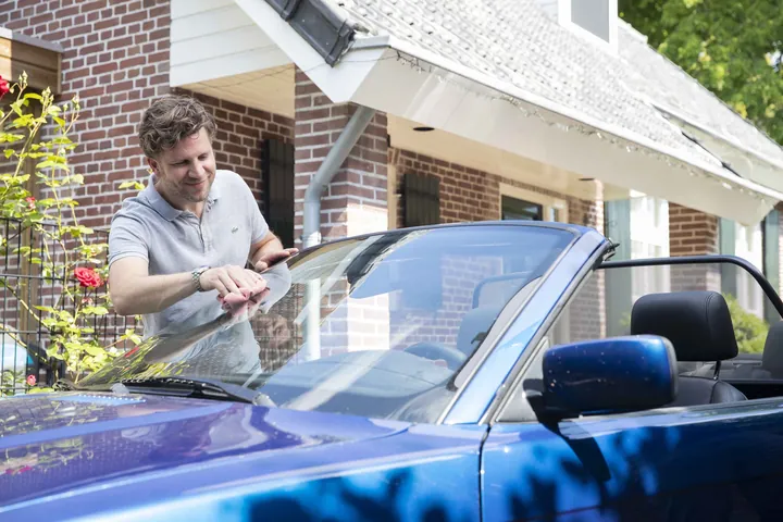 Roel bij een blauwe cabriolet voor een bakstenen huis