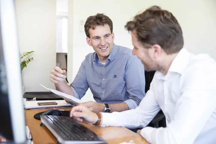 Erwin en Roel overleggen aan een bureau op kantoor