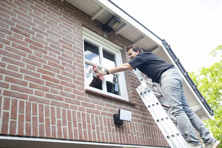Iemand van het kantoor zet op een ladder een raam van een bakstenen huis vast
